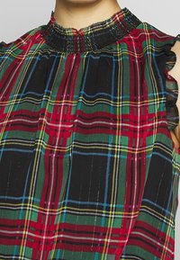 Haut en jersey avec encolure smockée, manches courtes et motif à carreaux rouge, vert, noir et bleu, avec un tissu texturé.