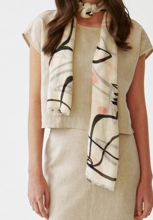 Femme portant une robe en lin beige à manches courtes avec une écharpe légère ornée de motifs abstraits en coups de pinceau noirs et roses.