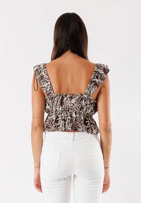 Top peplum marrone e bianco con motivo, maniche a volant e schiena profonda. Abbinato a jeans bianchi a vita alta.