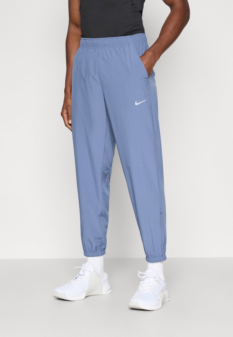 Světle modré sportovní tepláky vyrobené z hladkého materiálu, s elastickým pasem, bočními kapsami a malým bílým logem Nike.