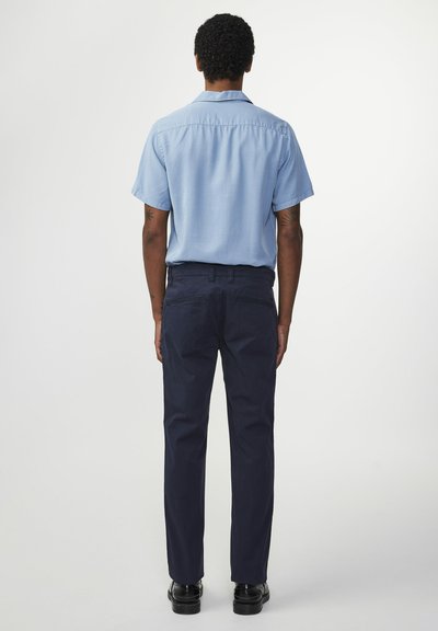 Camicia azzurro chiaro a maniche corte e pantaloni blu scuro, entrambi in tessuto liscio. Cuciture visibili e design a taglio dritto. Scarpe nere.