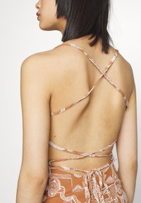 Vestido castanho com padrão, apresentando finas alças ajustáveis em um design cruzado nas costas, com um detalhe de laço na cintura.