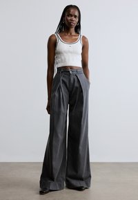 Šedé kalhoty s širokými nohavicemi vyrobené z měkké látky mají pás s opaskem a záhyby. Kombinovány s přiléhavým, texturovaným bílým krátkým topem.