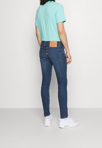Jeans pitillo de mezclilla azul oscuro con una parche de cuero en la parte trasera. Combinados con una camiseta de color turquesa claro y zapatillas deportivas blancas.