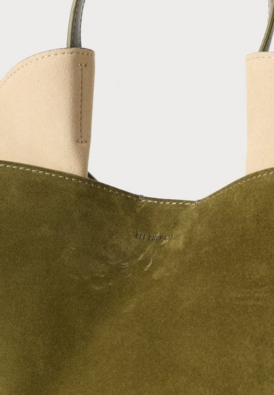 Sac tote en daim vert olive avec une ouverture en cuir beige, présentant une texture lisse, des coutures détaillées et un marquage en relief à l'intérieur.
