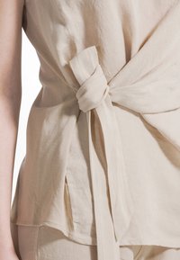 Beige top gemaakt van zachte stof, met een gestrikt detail aan de zijkant, een ontspannen pasvorm en een licht gestructureerd oppervlak.