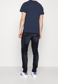 Marinblå t-shirt i fitted stil, kombinerad med mörkblå jeans. Outfitten kompletteras med vita skor med blå och röda ränder.