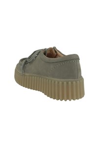Scarpe in suede grigio con punta arrotondata, cuciture rinforzate, dettaglio di allacciatura e una suola in gomma rigida di colore beige chiaro, spessa e a coste.
