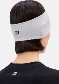 Grijze sporthoofdband met een gestructureerde afwerking, met een zwart logo. Wordt gedragen rond de achterkant van een hoofd met donker, steil haar.