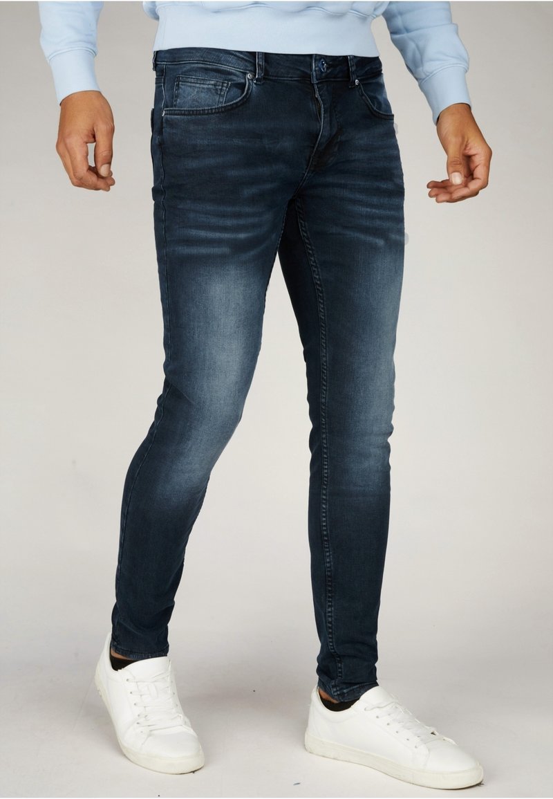 Tmavě modré úzké džíny vyrobené z denimu se slabým vyblednutím, pět kapes a zapínání na knoflík. Kombinované s bílými teniskami.