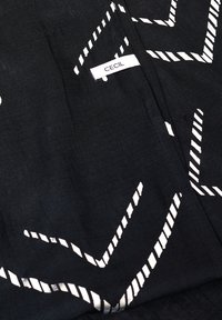 Tissu noir avec des motifs en zigzag et des rayures blanches, présentant une étiquette de marque visible "CECIL" cousue. Texture lisse.