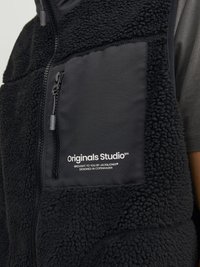 Chaleco de forro polar negro con un bolsillo de tela lisa, cierre de cremallera y marca. Presenta un exterior de forro polar texturizado y un diseño funcional.