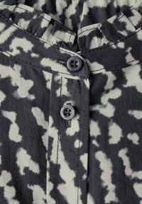 Camicia a bottoni con motivo astratto in bianco e nero, realizzata in tessuto testurizzato e con un singolo bottone scuro al colletto.