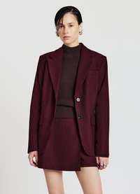 Blazer bordeaux a righe indossato sopra un top di maglia marrone, abbinato a una gonna coordinata. Il blazer ha due bottoni e tasche laterali.