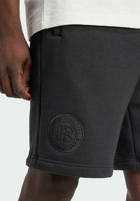 Shorts de sport noirs en mélange de coton, avec une étiquette en relief, des poches latérales et une taille élastique pour le confort et l'ajustement.