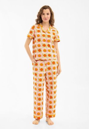 Woman standing barefoot wearing orange and pink floral patterned short-sleeve top and matching wide-leg pants against white background.