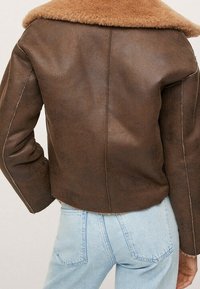 Veste en cuir marron avec large col en peau lainée beige portée sur un jean en denim bleu clair, vue de dos.