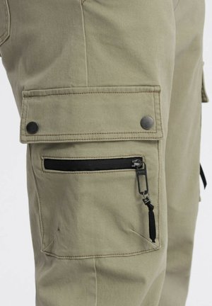 Cargo-broek in olijfgroen stof met een gladde textuur. Kenmerken zijn onder andere een zijzak met een zwarte ritssluiting en knoopsluiting.
