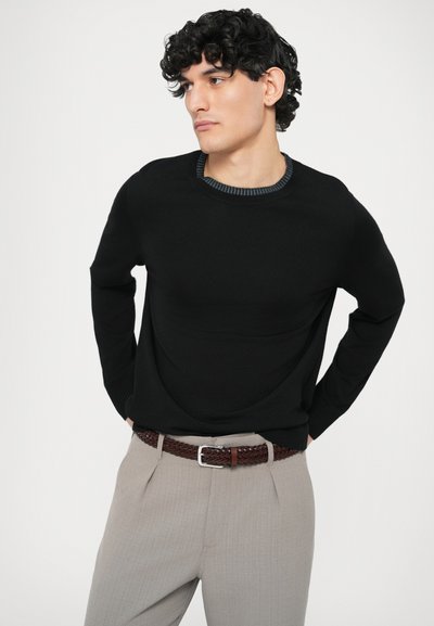 Czarny sweter z teksturowanym, prążkowanym dekoltem. Noszony z jasnoszarymi spodniami i brązowym plecionym paskiem. Prosty, dopasowany fason.