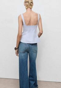 Helles blaues ärmelloses Top mit quadratischem Rückenteil, kombiniert mit weiten hellblauen Denim-Jeans mit Gesäßtaschen. Glatte Stoffstruktur.