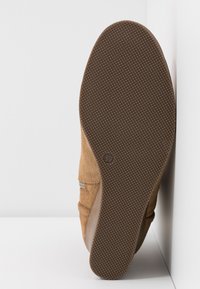 Semelle de chaussure en daim marron avec grip texturé, taille marquée 37, présentée en angle contre des coins blancs.