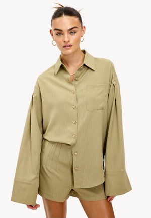 Chemise vert olive clair avec un col, des manches longues, des boutons dorés et une poche poitrine, assortie à un short avec des plis verticaux.