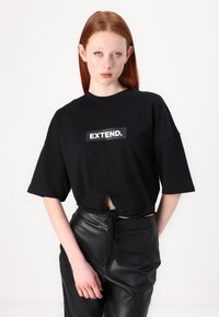 Melna īsām piedurknēm t-kreklu ar priekšējo mezglu un taisnstūra "EXTEND." grafiku baltā krāsā. Saskaņojot ar augsto vidukli melnām ādas biksēm.