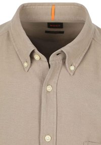 Beige overhemd met zachte textuur, korte kraag en witte knopen. Heeft een oranje accentsteek op de kraag.