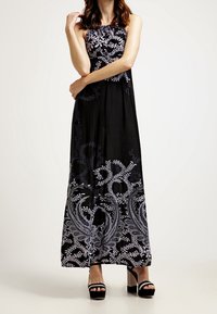 Svart maxiklänning med vitt blommönster och paisleymönster nertill. Har en axelbandslös design och ett mjukt, flödande tyg.