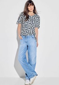 T-shirt i grå med fede, hvide bogstaver; parret med lyseblå, løstsiddende jeans og hvide sneakers.