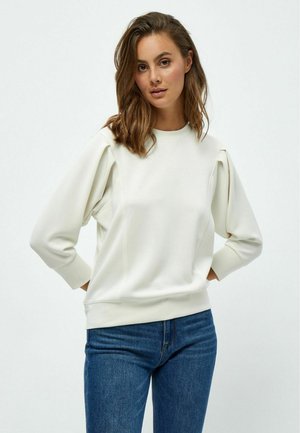 Svijetlosmeđa dugosvjetlana sweatshirts s detaljem na ramenima, rebrastim manžetama i opuštenim krojem. Uparen s plavim trapericama.
