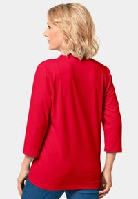 Rotes Langarm-T-Shirt aus weichem Stoff, mit Rundhalsausschnitt und lässiger Passform, kombiniert mit blauen Jeans.