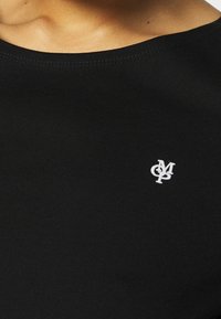 Černé bavlněné tričko s kulatým výstřihem, na levé části hrudi se nachází malé bílé vyšívané logo. Hladký povrch.
