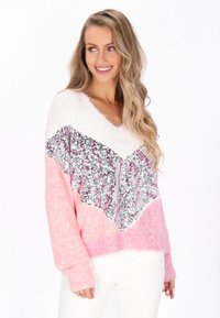 Jasnoróżowy, puszysty sweter z białym i srebrnym cekinowym wzorem w chevron. Posiada dekolt w kształcie V oraz długie rękawy. Matowa tekstura kontrastuje z cekinami.