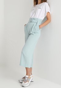 Light blue, high-waisted wide-leg trousers with pleats and a belted waist, paired with a white short-sleeve t-shirt featuring text.