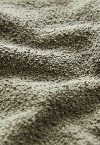 Teksturowana tkanina w kolorze oliwkowym z miękką, puszystą powierzchnią i małymi, ciasno splecionymi pętelkami. Materiał ma lekko nierówny, naturalny wygląd.