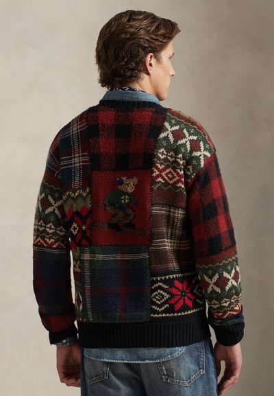 Stickad tröja med olika lapptäcksmönster i rött, grönt och blått rutigt, med ribbade muddar och fåll. Inkluderar ett broderat björndetalj.