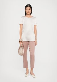 Top in satin beige chiaro con maniche corte, abbinato a pantaloni rosa cipria. Il modello tiene in mano una borsa beige e indossa tacchi bianchi a punta.