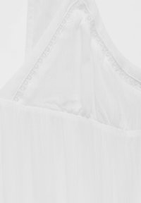 Haut blanc sans manches en tissu léger, avec un délicat bord en dentelle au niveau du col et une texture douce et fluide.