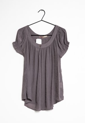 Grijze blouse met korte mouwen, gathered stof, ronde hals, twee knopen bij de kraag, hangend aan een zwarte draadhanger.