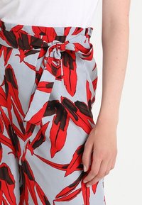 Lösa byxor i ljusblått tyg med ett iögonfallande mönster av röda och svarta löv. Midjebandet har en knutdetalj.