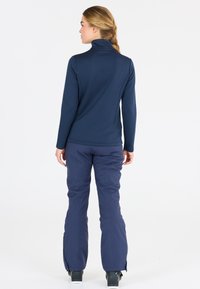 Marinblå långärmad topp med hög krage och strukturerad mönstring, i kombination med matchande marinblå byxor som har dragkedjor vid anklarna.