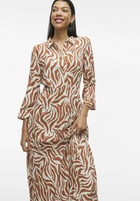 Robe longue à boutonner blanche avec des motifs en vagues marron. Présente des manches longues et un col, fabriquée en tissu léger et lisse.