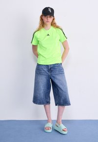 Neonsko zelena sportska majica, traper burberry hlače i zeleni klizni sandali; kapa s logom, ležeran kroj i kontrastne pruge na rukavima.