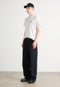 Hvid bomulds t-shirt med lille sort tekst, mørkeblå løse jeans og sort cap. Sorte sko med tykkere sål. Enkel, afslappet design.
