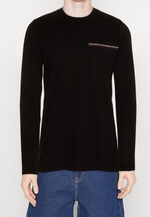 Sort langærmet T-shirt lavet af bomuld, med en lille rød og hvid tekstgrafik på venstre brystområde og rund halsudskæring.