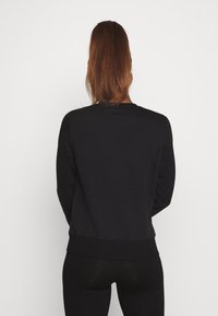 Sudadera negra con mangas largas, escote redondeado y dobladillo acanalado. La tela parece suave y elástica.