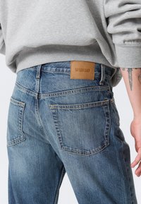 Ανοιχτό μπλε τζιν παντελόνι με δερμάτινο λογότυπο "WEEKDAY", διακριτική ξεθώριαση, πορτοκαλί ραφές και κανονικές πίσω τσέπες.