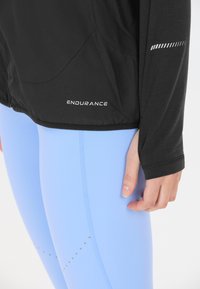 Svart långärmad topp med "ENDURANCE" logotyp, kombinerad med ljusblå tights med subtila prickmönster och en mjuk, stretchig textur.