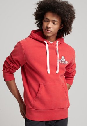 Felpa rossa con cappuccio, dotata di tasca a marsupio sul davanti, cordini bianchi e logo "Superdry". Realizzata in tessuto morbido con polsini e orlo a coste.